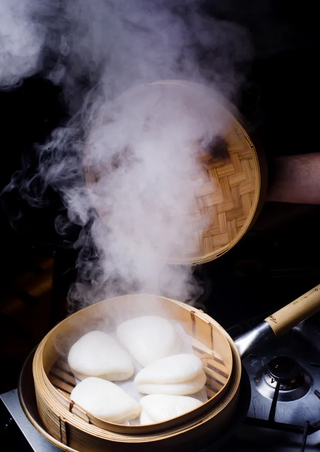 Freshly steamed bao buns in a bamboo steamer with steam rising